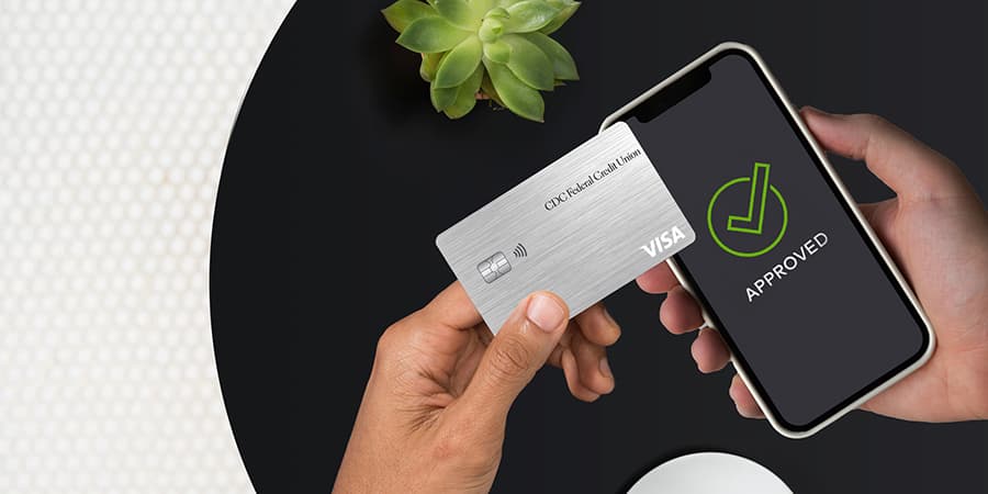 Hands holding a credit card and a smartphone showing a green checkmark on the screen with the words approved.