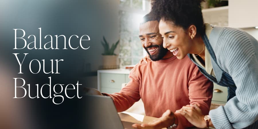 A happy African American couple looking at a laptop screen. The words at the left: balance your budget.