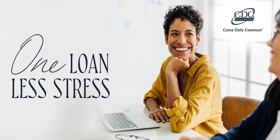 A smiling woman sitting at her desk looking at another woman beside her. The words at the left: one loan less stress.