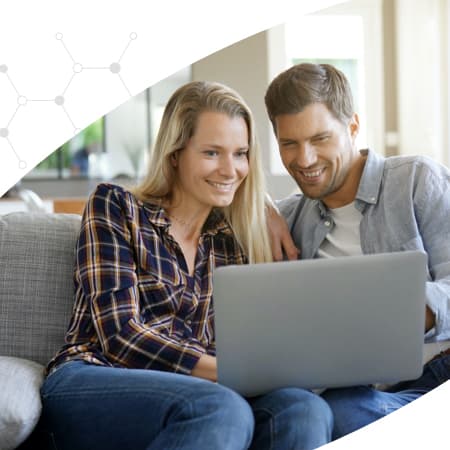 A couple sitting on a couch looking at a laptop.