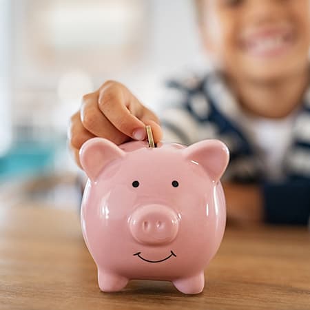 A young boy depositing a coin into a pink piggy bank.
