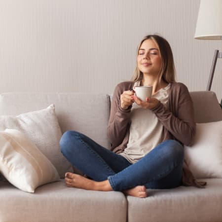 A woman relaxing while sitting on a couch drinking coffee.
