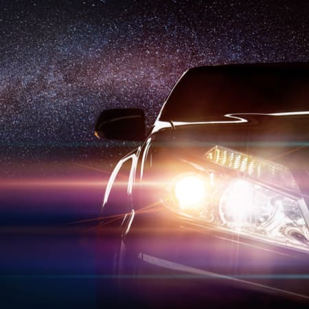 An up-close view of the headlights of a sports car against a night sky.