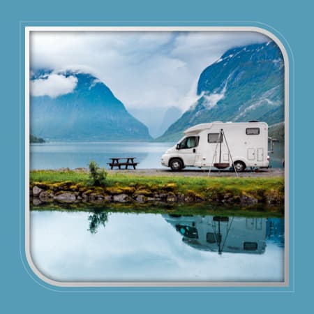 An RV parked on the shoreline of a beautiful lake in between mountains.