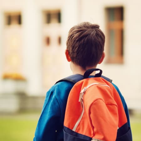 A young boy wearing a bright, orange back pack.