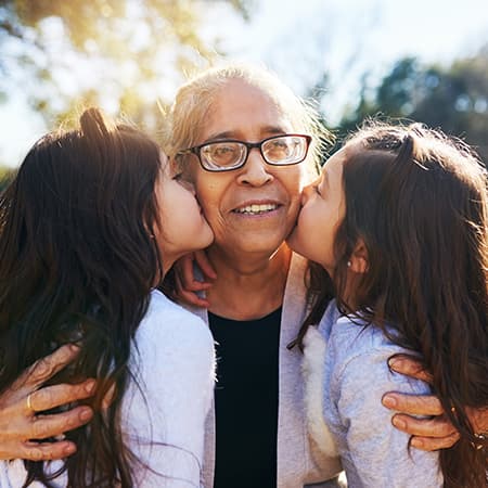 Two young girls hugging and kissing an elderly woman.