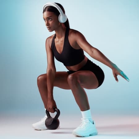 Woman in workout clothes with headphones squatting with a kettlebell.