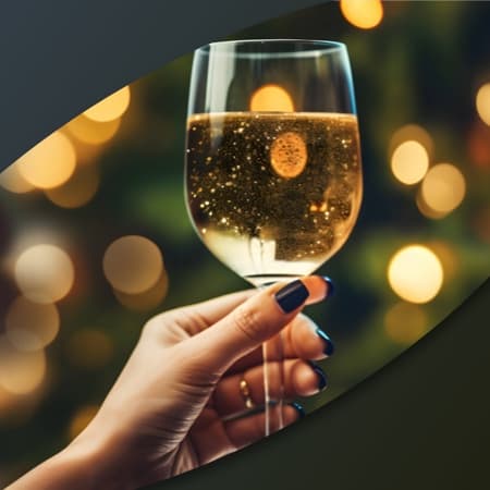 A woman's hand holding a glass of champagne with twinkling lights in the background.