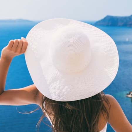 A woman with a white hat gazing out into the ocean.