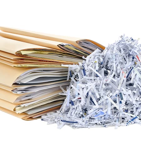 A pile of Shredded paper next to folders filled with documents.