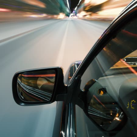 The side profile of a car driving at night with focus on the rearview mirror.