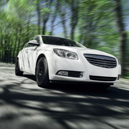 A white luxury vehicle driving down a tree lined street.