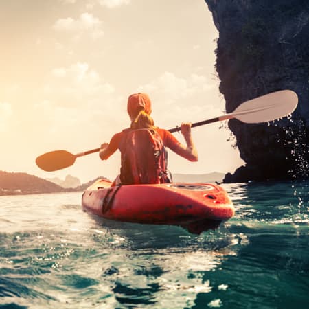 A woman kayaking along a beautiful cliff lined beach.