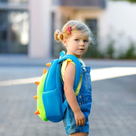 A cute little blonde girl with a book bag.