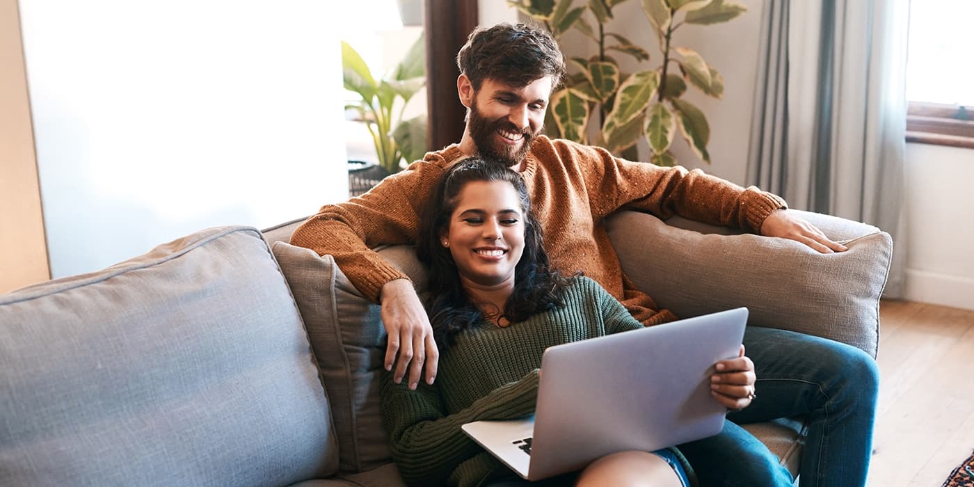 A young couple sitting on a couch while looking at a laptop.
