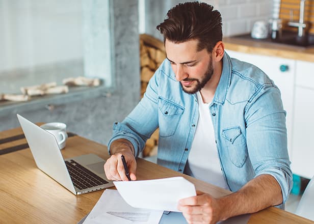 A young man sitting at a kitchen counter using a laptop.