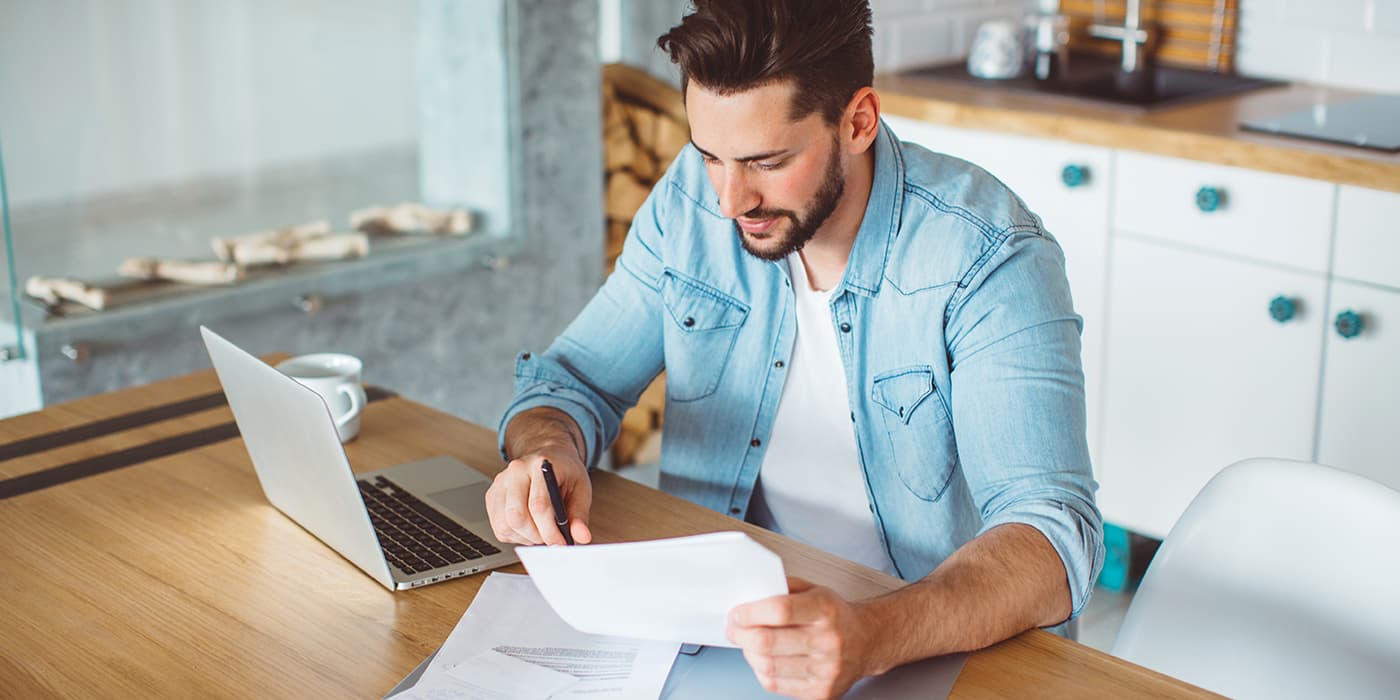 A young man sitting at a kitchen counter using a laptop.