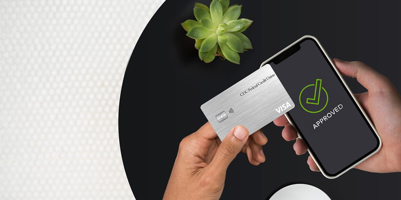 Hands holding a credit card and a smartphone showing a green checkmark on the screen with the words approved.