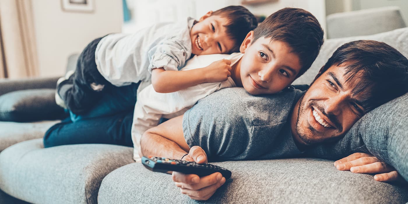 A father laying on a couch with two young boys on his back.