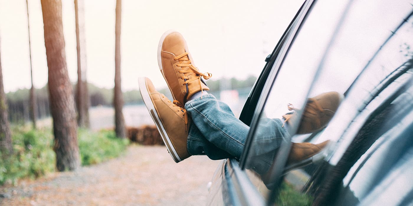 A person sitting comfortably in a car with their feet outside the window.