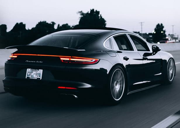A grayscale picture of a porsche sedan driving on the highway.
