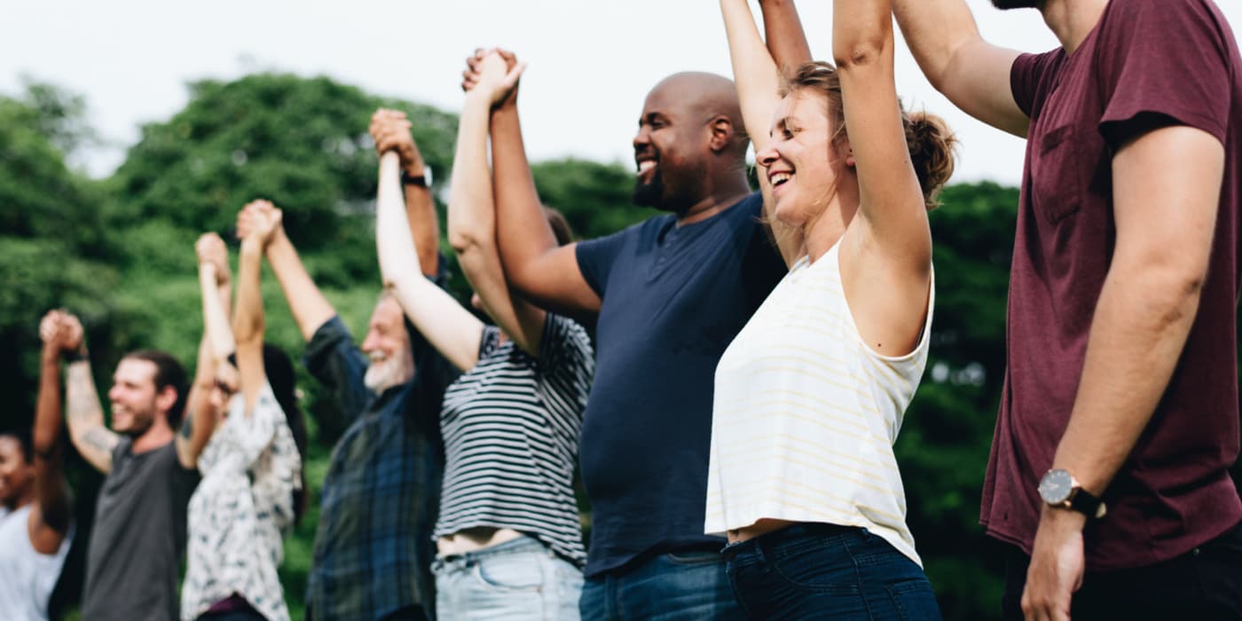 Diverse group of people standing outdoors holding hands and raising their arms together in celebration.