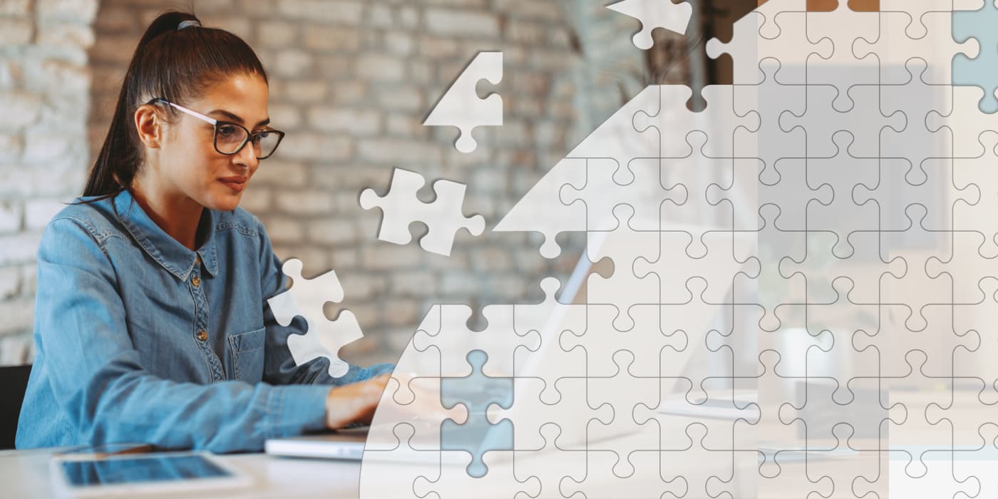 A world map made up of puzzle pieces. In the background, a young woman using a laptop.