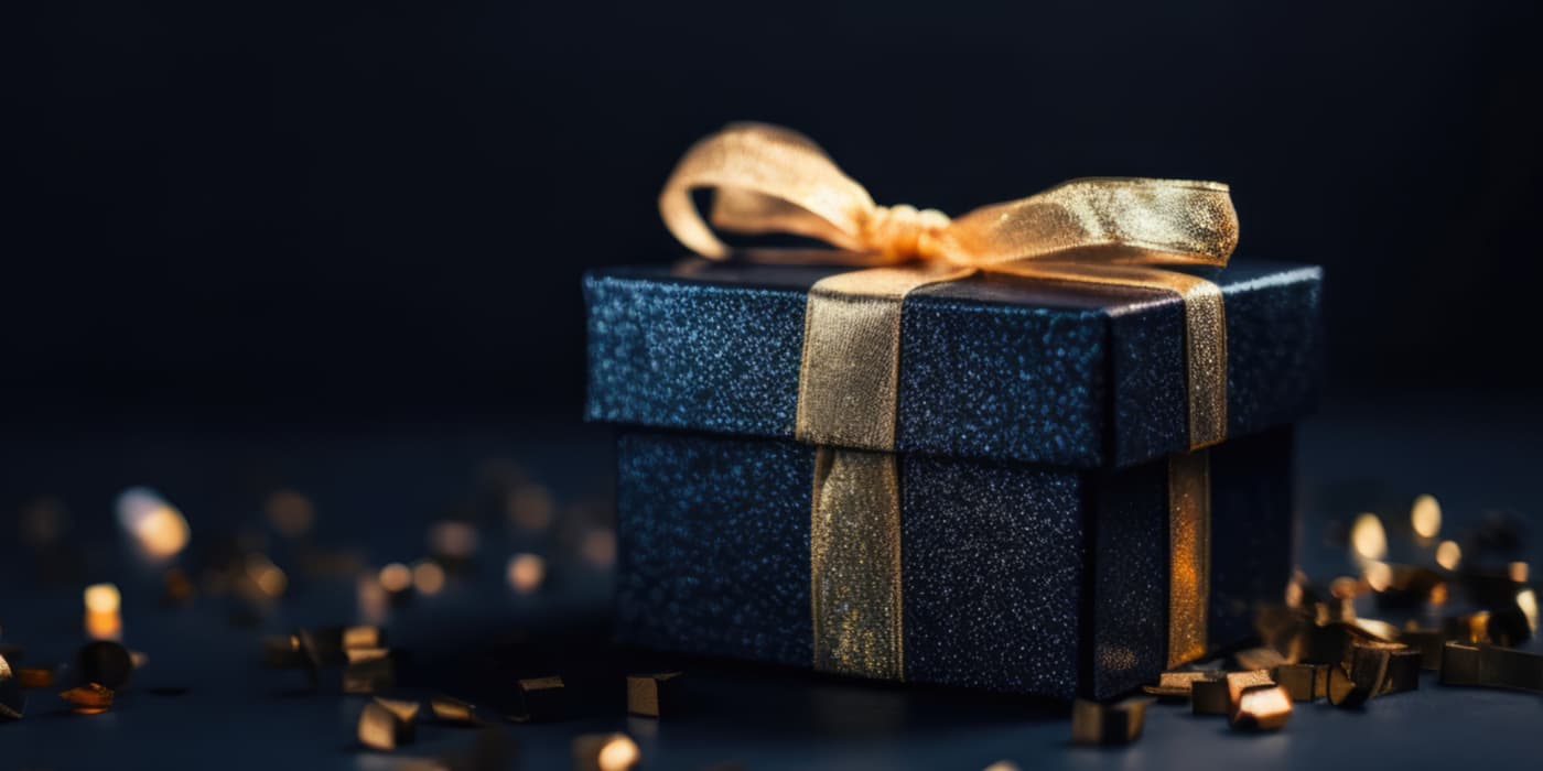 A beautifully wrapped navy box with a gold ribbon surrounded by gold confetti.