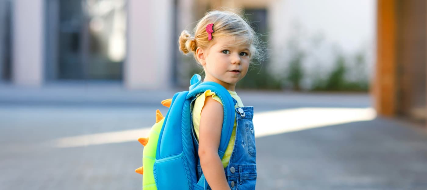 A cute little blonde girl with a book bag.