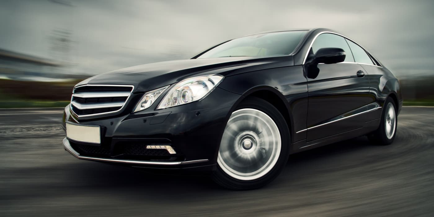 Black luxury sedan driving on a roadway with motion blur, conveying speed and performance.