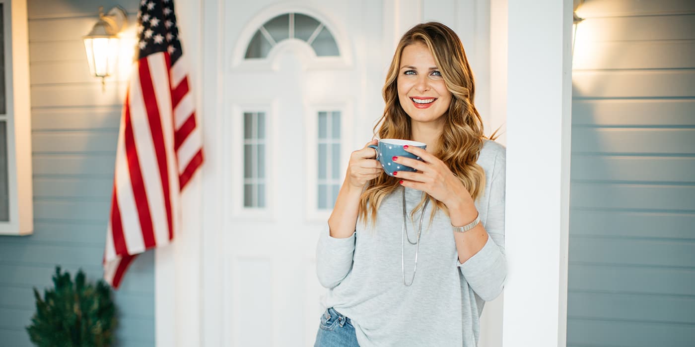 A young woman standing on a porch while holding a coffee mug.