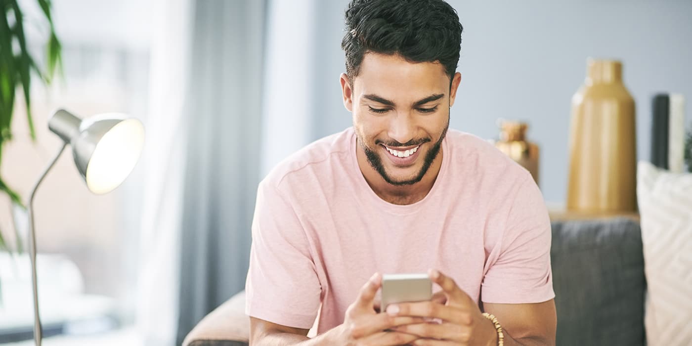A young man sitting on a couch using a smartphone.