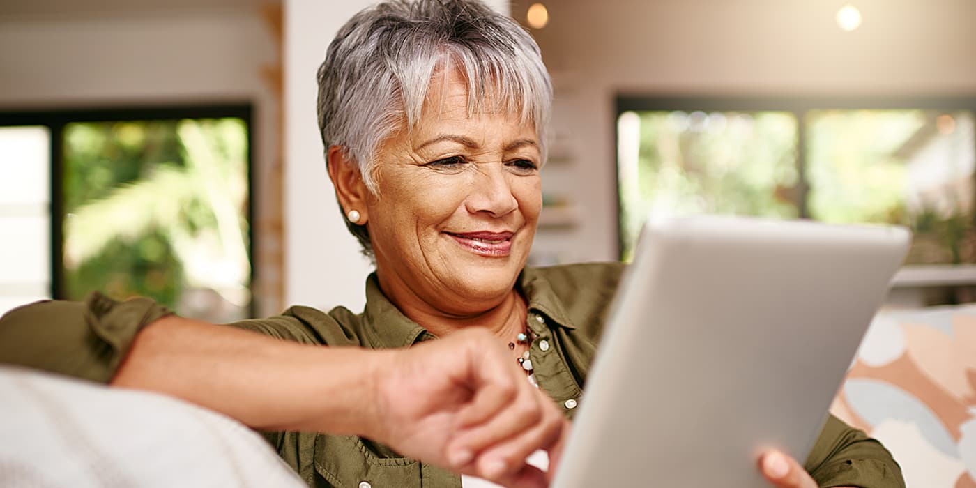 An elderly woman sitting on a couch using a tablet.
